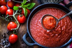 Pentola con dentro molto sugo con intorno sul tavolo alcuni pomodori
